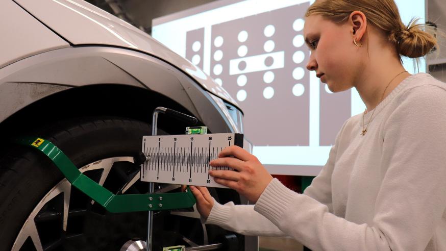 Student measuring a car wheel alignment in an automotive engineering laboratory