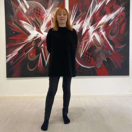 Muotoilun alumni Matilda Hööpakka mustissa vaatteissa kuvattuna punamustavalkoisen taideteoksen edessä.